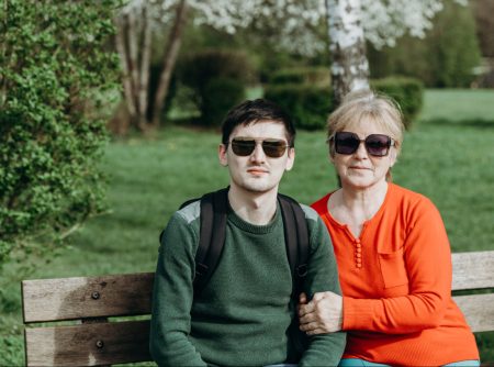 mother and adult son sitting outside on a bench