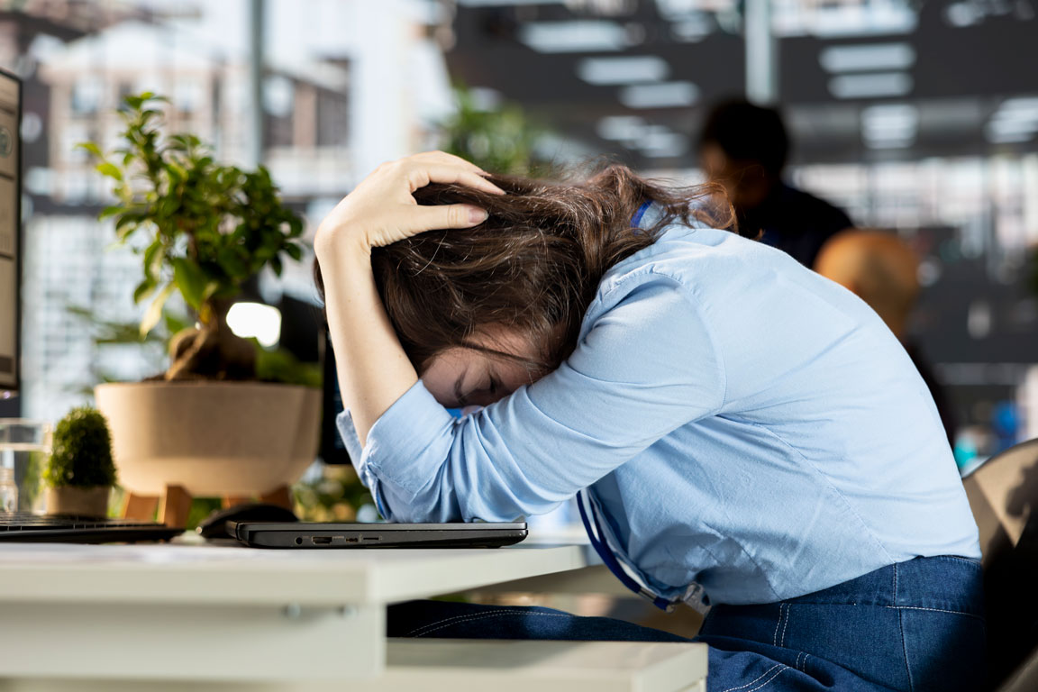 stressed-woman-with-head-in-hands-in-office woman upset on her desk